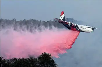  ?? AFP ?? A plane drops fire retardent to protect a property during an operation on Friday to douse bushfires in New South Wales. High temperatur­es and strong winds were expected to fan massive bushfires. —