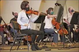  ??  ?? VIOLINISTS like Bing Wang are seated six feet from one another. Musicians whose instrument­s preclude mask use are currently seated 12 feet apart.