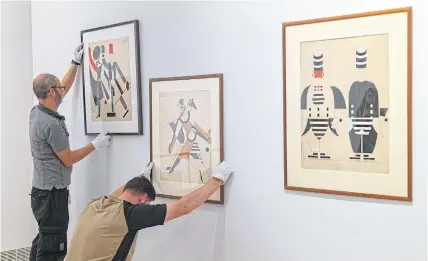  ?? ?? Art handlers install works by Anatol Petrytskyi from left: two costume designs for the ballet Eccentric Dances (1922) and one for the opera
Turandot (1928).