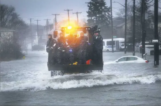  ?? Gary Higgins/The Quincy Patriot Ledger via AP ?? A front-end loader is used to transport a Marine rescue team along a flooded street Friday in Quincy, Mass.