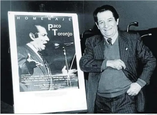  ?? H. INFORMACIÓ­N ?? Paco Toronjo sonríe, posando junto a un cartel de uno de sus homenajes, en 1998.