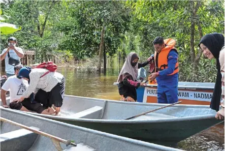  ?? ?? Emergency backup: Civil defence Force members helping ferry flood victims to the polling station at Kampung Tersang in rantau Panjang. — bernama