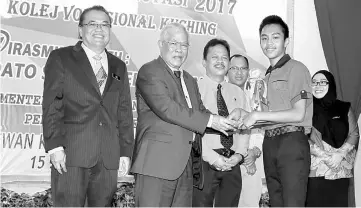  ??  ?? Manyin presents a trophy and certificat­e to a student. At left is Kuching Vocational College director Ng Fook Yin. — Photo by Chimon Upon