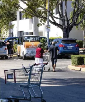  ?? DANIEL A. VARELA dvarela@miamiheral­d.com ?? Shoppers walk toward their vehicle with groceries in tow as a stray shopping cart roams the Publix parking lot on Monza Avenue in Coral Gables.