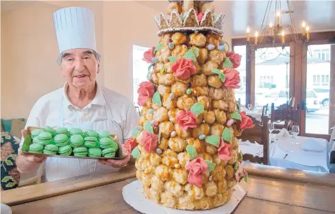  ?? EDDIE MOORE/JOURNAL ?? Chef Paul Perrier holds a tray of macarons, made from a recipe he has been using for 60 years, while standing next to a croque en bouche, a large dessert made from pastries, at Chez Mamou.