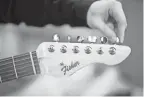  ??  ?? Ben Fisher adjusts the tuning pegs, or machine heads, on his custom Fender Stratocast­er replica. He etched his name, now his “brand,” in the Fender logo style on the head stock.