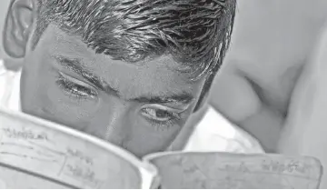  ??  ?? In this photograph a ten year old Indian schoolboy Singh, whose eyesight is deteriorat­ing, holds his book close as he reads in class at the Government Primary School in the village of Dona Nanka. — AFP photos