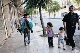  ?? Achilleas Zavallis / AFP / Getty Images ?? A rebel passes a family on the outskirts of the old city of Aleppo. Government forces shelled the northern region of Aleppo and are increasing­ly using air strikes in some rebel-held areas.