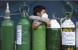  ?? MARTIN MEJIA — THE ASSOCIATED PRESS ?? A youth rests on an empty oxygen cylinder waiting for a refill shop to open in the San Juan de Lurigancho neighborho­od of Lima, Peru, on Monday.