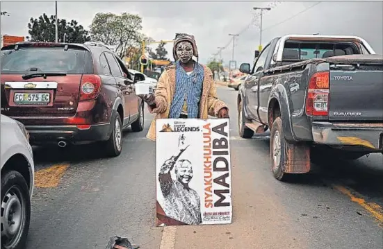  ?? CARL DE SOUZA / AFP ?? Un niño sostiene un póster con la imagen de Mandela mientras mendiga en las calles de Mthata, cerca de Qunu, donde nació Madiba