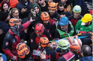  ?? The Associated Press ?? ■ Raziye Kilinc is carried through a crowd on a stretcher after she was rescued under a destroyed building as her daughter, center, with the green black hood, waves in Iskenderun, southeaste­rn Turkey, on Feb. 10. Ever since the powerful 7.8 earthquake that has become Turkey’s deadliest disaster in modern history, survivors have been gathering outside destroyed buildings, refusing to leave.