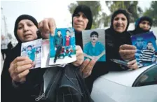  ?? THE ASSOCIATED PRESS ?? Women show photos of relatives at Nineveh Criminal Court, one of two counterter­rorism courts in Iraq where suspected Islamic State militants and their associates are tried, in Tel Keif, Iraq.