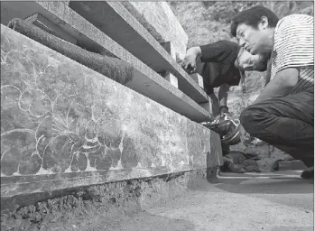  ?? CHENG GONG / FOR CHINA DAILY ?? Archaeolog­ists study the cover and base of the inscriptio­n stone for the wife of Liu Ji, a major military governor during the Tang Dynasty (AD 618-907). The base has peony patterns.