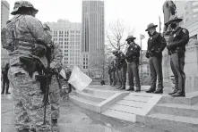  ??  ?? Ohio state troopers provide security Sunday at the Ohio Statehouse as armed protestors look on, in Columbus, Ohio. Security was stepped up at statehouse­s across the U.S. after FBI warnings of potential armed protests at all 50 state capitols and in Washington, D.C. [JAY LAPRETE/ THE ASSOCIATED PRESS]