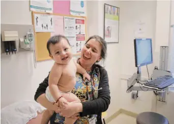  ?? Carlos Avila Gonzalez/The Chronicle 2017 ?? Dr. Erin Gonzales holds a baby during a checkup at La Clinica de La Raza in Oakland in 2017. California is weighing new continuous-enrollment policies for the youngest Medicaid members.