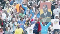  ?? — Reuters ?? Supporters of Zimbabwe’s President Robert Mugabe hold a poster with his picture as he addresses mourners gathered for the burial of National Hero Charles Utete at the Heroes Acre in Harare, Zimbabwe, recently.