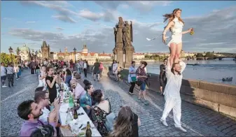  ?? GABRIEL KUCHTA / GETTY IMAGES ?? A couple perform as residents dine at a 500-meter-long table set on the Charles Bridge in Prague on Tuesday, after coronaviru­s restrictio­ns were eased in the Czech capital. Some 2,000 seats were available with people invited to bring and share food and drinks to welcome the summer.