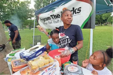  ?? ANGELA PETERSON / MILWAUKEE JOURNAL SENTINEL ?? Bobbie Wright (left), 10, and Mariah Kyles, 7, stay close to Gabriel Taylor, who is helping Vaun Mayes (far left) prepare food at Sherman Park for residents on Aug. 2. “If they see that you care about them, they will open up to you. One meal can change...