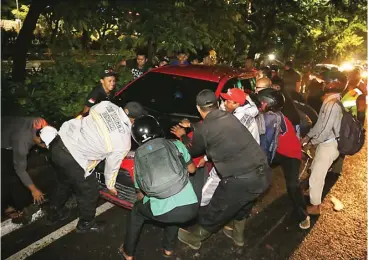  ?? DITE SURENDRA/JAWA POS ?? BANTING SETIR: Petugas dishub dibantu warga mengeluark­an mobil Alexander T. Wijarno dari gorong-gorong di Jalan A. Yani, kemarin dini hari.