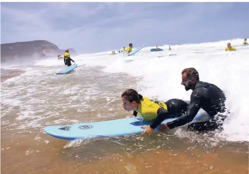  ?? FOTOS: MEYER/DPA ?? Ab in die Wellen: Surflehrer Hugo hilft einer Schülerin an der Praia da Cordoama.