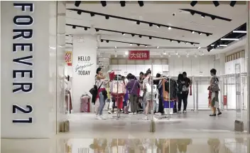  ?? AP FOTO ?? Women select clothing at Forever 21, which is offering clearance discounts at a shopping mall in Beijing, China. Forever 21 has filed for bankruptcy amid changing consumer tastes.