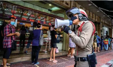  ??  ?? A police officer enforces social distancing as people wearing face masks amid fears of the spread of Covid-19 coronaviru­s line up to sell their jewellerie­s in front of a gold shop in Bangkok’s Chinatown yesterday.