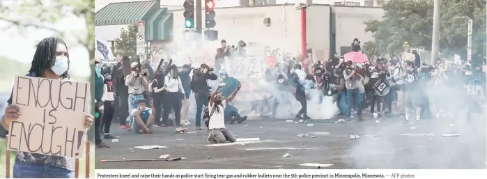  ?? — AFP photos ?? Protesters kneel and raise their hands as police start firing tear gas and rubber bullets near the 5th police precinct in Minneapoli­s, Minnesota.