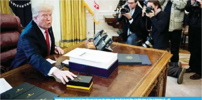  ?? —AFP ?? WASHINGTON DC: US President Donald Trump offers pens to the press after signing a tax reform bill in the Oval Office of the White House on Friday in Washington, DC.