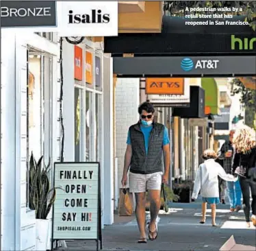  ??  ?? A pedestrian walks by a retail store that has reopened in San Francisco.