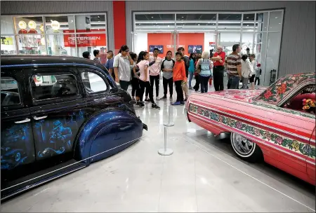  ?? AP/JAE C. HONG ?? Visitors examine a 1939 Chevrolet Master Deluxe named Gangster Squad ’39, (left) and Jesse Valadez’s Gypsy Rose, a customized 1964 Chevrolet Impala, during “The High Art of Riding Low” at the Petersen Automotive Museum in Los Angeles. The exhibition...