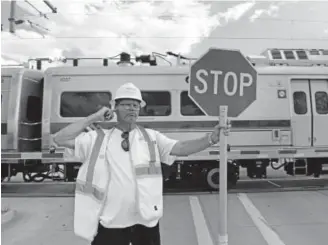  ?? Helen H. Richardson, The Denver Post ?? Flagger David Christ puts his finger in his ear to keep out the sound of the train horn as he holds up a stop sign at the A-Line railroad crossing at York Street between East 40th and East 41st avenues on Monday in Denver.