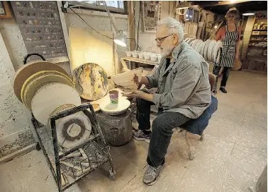  ??  ?? Richard Selfridge works on pottery in their basement studio, known as the throwing and glazing room, not far away from the corner where Carol is working. Above, Carol adds colour to a line of pottery, surrounded by photos of her favourite art form. .