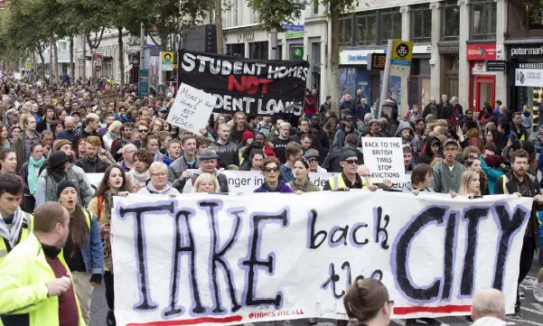  ??  ?? PROTEST: The Take Back The City campaigner­s march along O’Connell Street, (above) before occupying the LUAS line across the bridge (far left). Motherof-seven Margaret Cash addresses the crowd (left) and a protester displays a banner (inset below) Photos: Tony Gavin