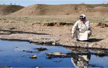  ?? ?? An Iraqi farmer squats and checks an oil spill into an agricultur­al land.
