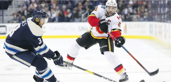  ?? PHOTOS: JAY LAPRETE/THE ASSOCIATED PRESS ?? Flames captain Mark Giordano dumps the puck past Seth Jones of the Blue Jackets during the first period on Tuesday night in Columbus, Ohio.