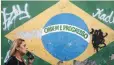  ??  ?? A woman talks on a phone passing a wall showing Brazil’s motto ‘Ordem e progresso’. — Reuters