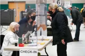  ?? AP PHOTO/STEVEN SENNE ?? In 2020, a poll worker, center left, speaks through a plastic barrier while assisting a voter in a polling station at Marshfield High School in Marshfield, Mass.