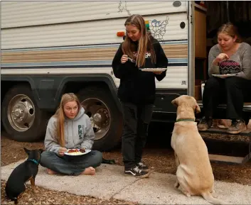  ?? AP PHOTO/JOHN LOCHER ?? In this 2018 file photo, sisters Arissa Harvey (from left) Araya Cipollini, and Arianne Harvey eat beside an RV they are living in near their home, which was was destroyed in the Camp Fire in Paradise, Calif.