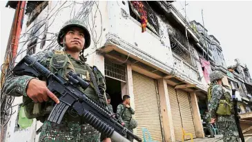  ?? — Reuters ?? On the alert: Government soldiers standing guard in front of damaged building and houses in Sultan Omar Dianalan boulevard at Mapandi district.