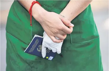  ?? REUTERS ?? A migrant worker holds a passport as she queues to talk with health officials after the recent Covid-19 outbreak at a market in Samut Sakhon.