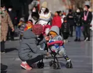  ?? AP PHOTO/ANDY WONG ?? A woman feeds a snack to a child Tuesday at Qianmen pedestrian shopping street, a popular tourist spot in Beijing.