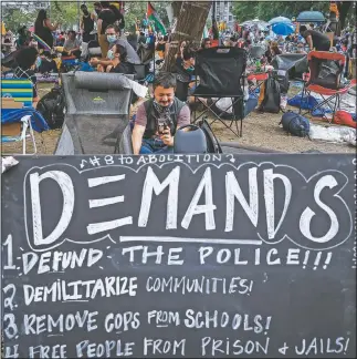  ?? (AP/John Minchillo) ?? Protesters rest Friday in a grassy area surrounded by signs calling for changes to police policies and practices at an encampment outside City Hall in New York.