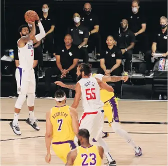  ??  ?? With the physically-distanced Los Angeles Clippers coaching staff in the background, forward Marcus Morris Sr. shoots against the Lakers during their first game of the NBA restart Thursday in Lake Buena Vista, Florida. The Lakers edged the Clippers 103-101.