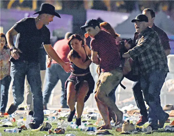  ??  ?? Concert-goers help carry a wounded person to safety during the massacre in Las Vegas carried out by Stephen Paddock, who used a legally bought arsenal of up to 20 weapons to kill at least 59 and leave 527 more injured