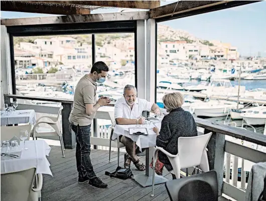  ?? DANIEL COLE/AP ?? A waiter wearing a face mask to protect from the coronaviru­s serves diners at a seafood restaurant June 2 in Marseille, southern France.