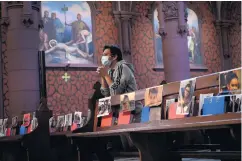  ??  ?? A man wearing a protective face mask prays in the Basilica of Neuchatel which displays the portraits of 400 parishione­rs unable to attend mass due