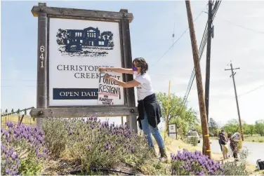  ?? Photos by Marlena Sloss / Special to The Chronicle ?? At a rally outside the Christophe­r Creek Winery near Healdsburg, Hollie Clausen of Santa Rosa hangs a sign demanding Windsor Mayor Dominic Foppoli step down. The winery is owned by the Foppoli family.