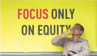  ??  ?? An Indian man drinks in front of an advertisem­ent for investment­s at a bus stop in Mumbai on February 8, 2018. Traders are struggling to get a firm footing in a volatile February, spooked by heavy selling and warnings of more upheaval to come.