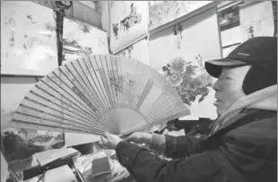  ??  ?? Jin demonstrat­es a calendar printed on a Chinese fan at his shop.