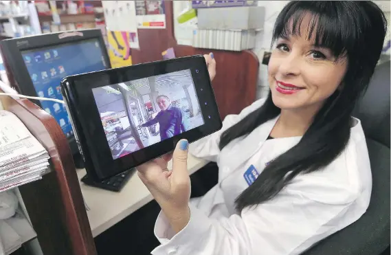  ?? DAN JANISSE ?? Marilyn Adamo of the Lifestyle Pharmacy displays a monitor that shows her husband Peter Adamo at the front entrance. The front doors are now locked at all times.